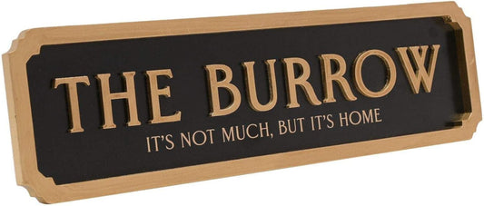 A rectangular wooden sign with a black face and raised gold lettering that reads “THE BURROW” with the smaller phrase “IT’S NOT MUCH, BUT IT’S HOME” below, shown on a plain white background.
