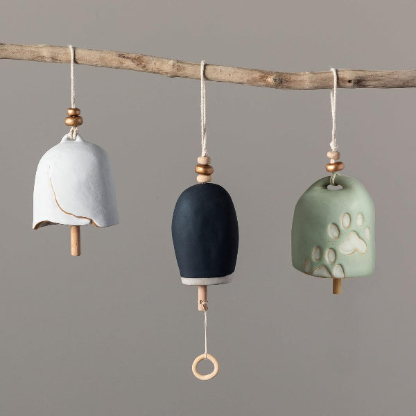 Three ceramic bells with wooden accents hanging from a branch against a gray background