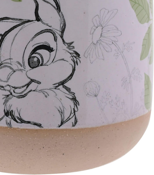 Ceramic mug with a cartoon character and floral design on a light purple background.