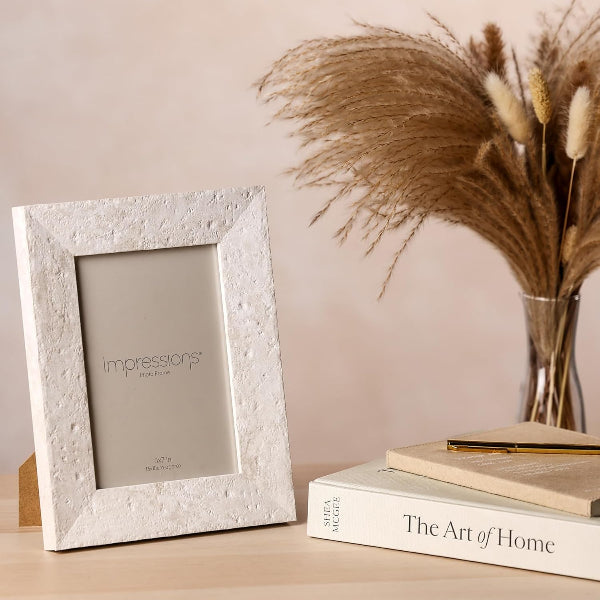 White textured picture frame on a surface with books and dried plants in the background