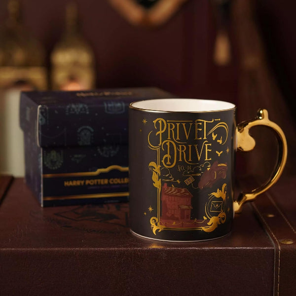 A dark navy blue Harry Potter collectible mug with gold foil detailing reading 'Privet Drive Vol. 1' and a gold handle, shown next to its branded box on a brown leather surface.