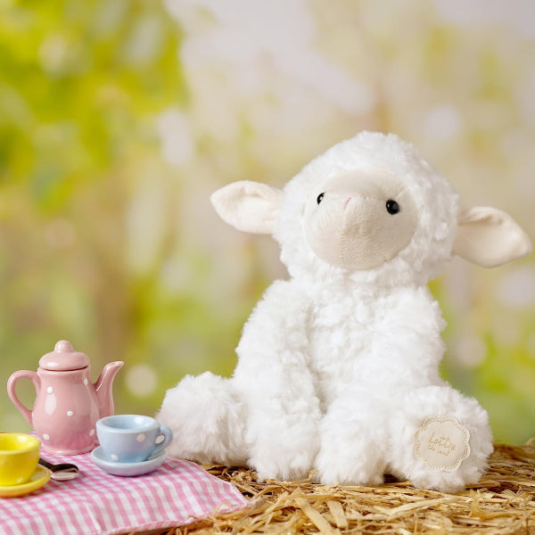 Plush lamb toy with a tea set on a checkered cloth against a blurred natural background