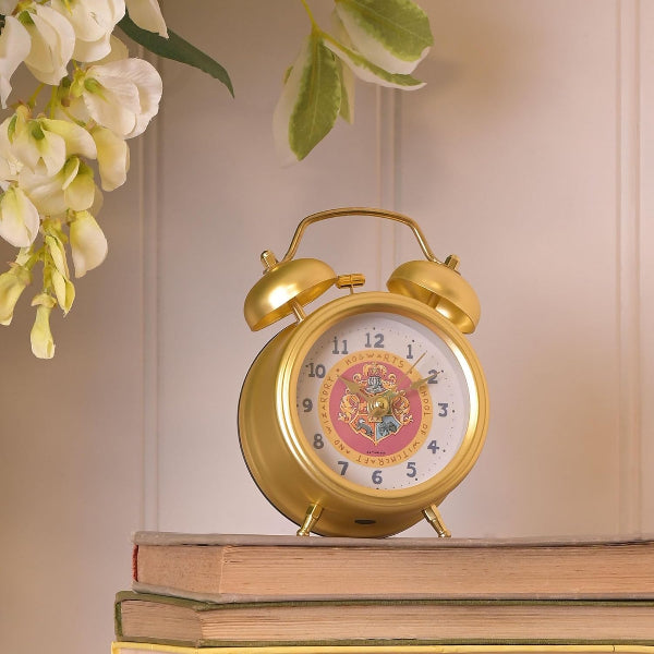 Gold alarm clock with decorative face on a stack of books, surrounded by flowers.