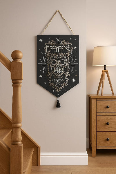 Decorative banner with skull design and 'Morsmordre' text hanging on a wall next to a wooden staircase and lamp.