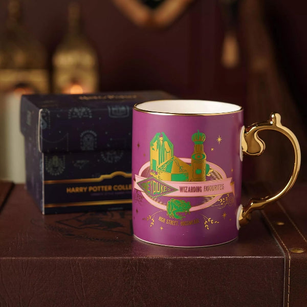 A purple Harry Potter collectible mug with a gold handle and printed Hogwarts crest, shown next to its dark blue presentation box on a brown leather surface.