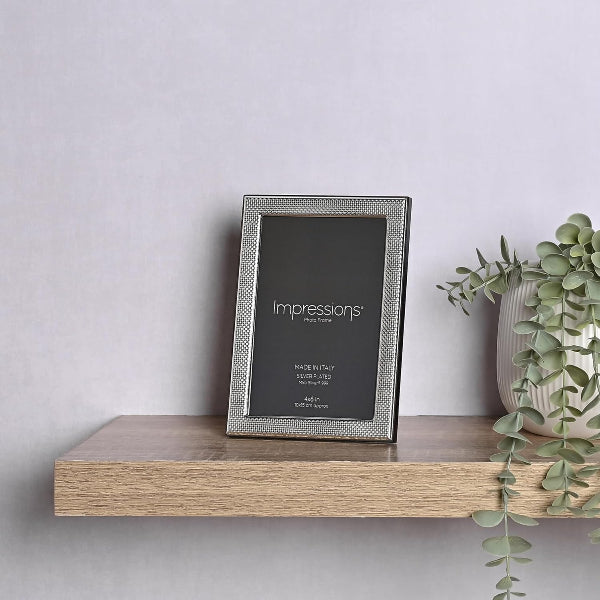 Silver photo frame with 'Impressions' branding on a wooden shelf against a light gray wall