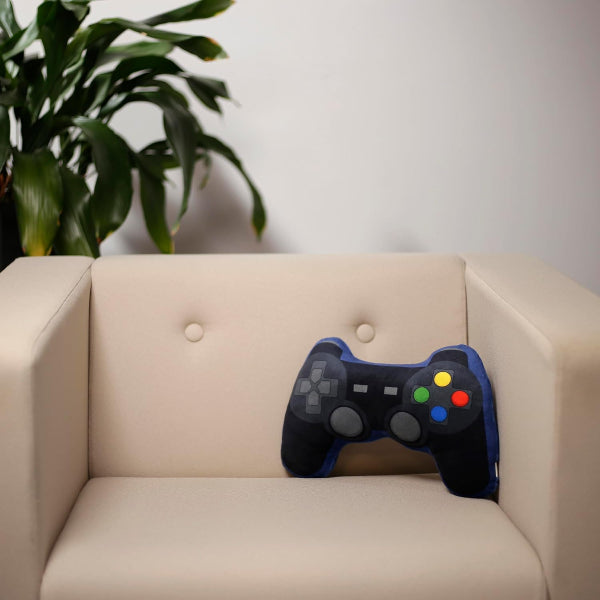 Game controller-shaped pillow on a beige couch with a plant in the background