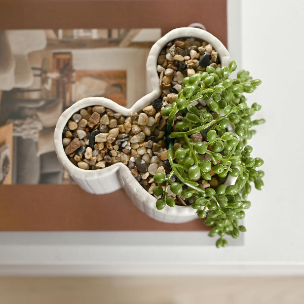 Heart-shaped ceramic planter with succulent plant and pebbles on a blurred background