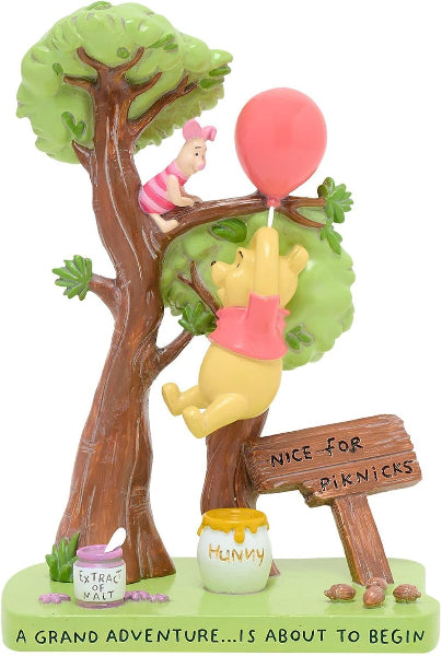 A Winnie the Pooh-themed decorative figurine showing Pooh climbing a tree while holding a pink balloon, with Piglet sitting on a branch, a honey pot labeled 'HUNNY,' a jar labeled 'EXTRACT OF MALT,' and a sign reading 'NICE FOR PICKNICS.'.