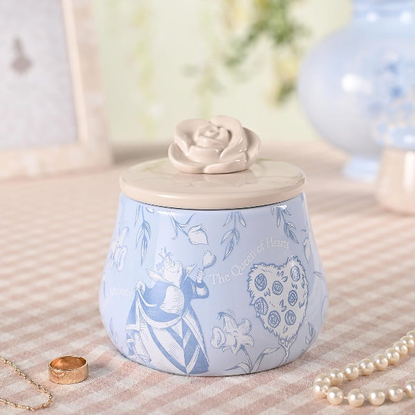 Decorative jar with a rose-shaped lid on a textured surface with jewelry.