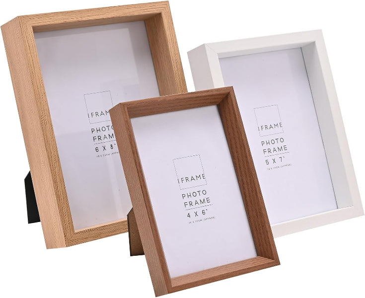 Three picture frames shown on a white background: two natural wood frames in the foreground and one white frame behind them. The front wood frame is angled and larger in prominence, with the other two frames partially overlapping behind it.