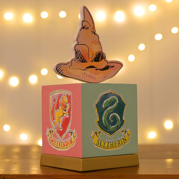 Decorative box with Gryffindor and Slytherin logos on a wooden surface with fairy lights in the background.