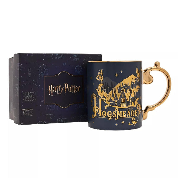A dark navy blue Harry Potter Pogsmeada mug with a gold handle and gold castle illustration, shown next to its branded dark blue gift box on a white background.