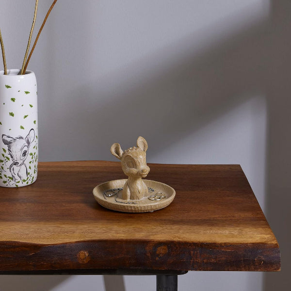 Ceramic deer figurine on a wooden table with a white vase featuring animal design in the background.
