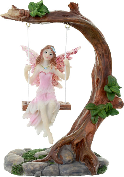 Fairy figurine on a swing attached to a tree branch with leaves and rocks on a white background