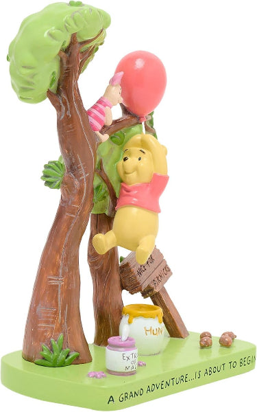 A Winnie the Pooh figurine showing Pooh climbing a tree and reaching for a pink balloon, with Piglet on a branch above, a honey pot, and a green base that reads 'A GRAND ADVENTURE.