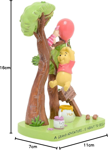 A Winnie the Pooh treehouse figurine on a light green base, featuring Pooh climbing a tree with a pink balloon, a small figure in a pink outfit, honey pots, and dimension markings showing 16cm height, 7cm width, and 11cm depth.