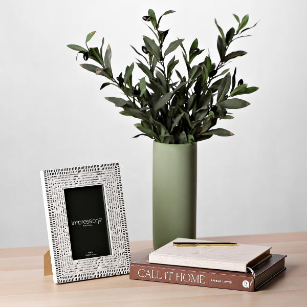 Vase with greenery, photo frame, and books on a wooden surface
