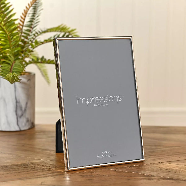 Silver photo frame with 'Impressions' branding on a wooden surface with a plant in the background.