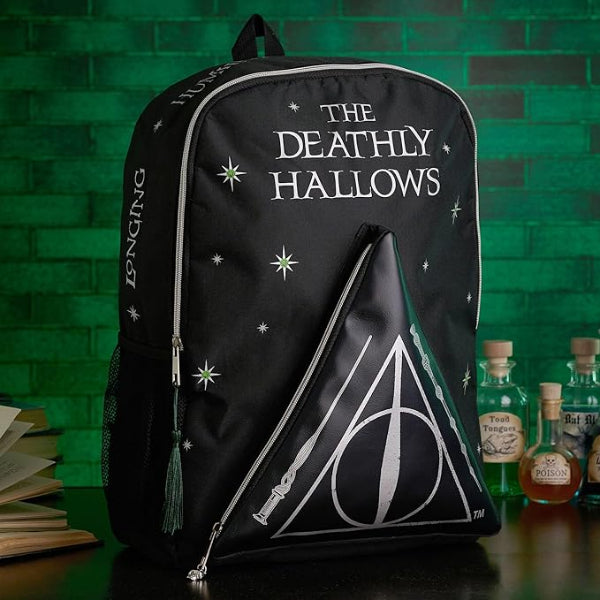 Black backpack with 'The Deathly Hallows' text and design, placed against a green brick wall with potion bottles.
