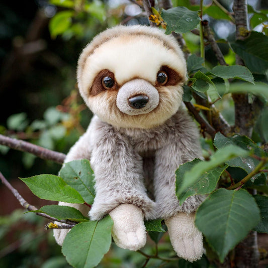 Stuffed sloth toy in a tree with green leaves