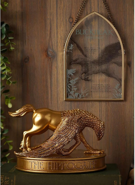 Gold hippocampus figurine on a wooden surface with a framed picture of a squirrel in the background.