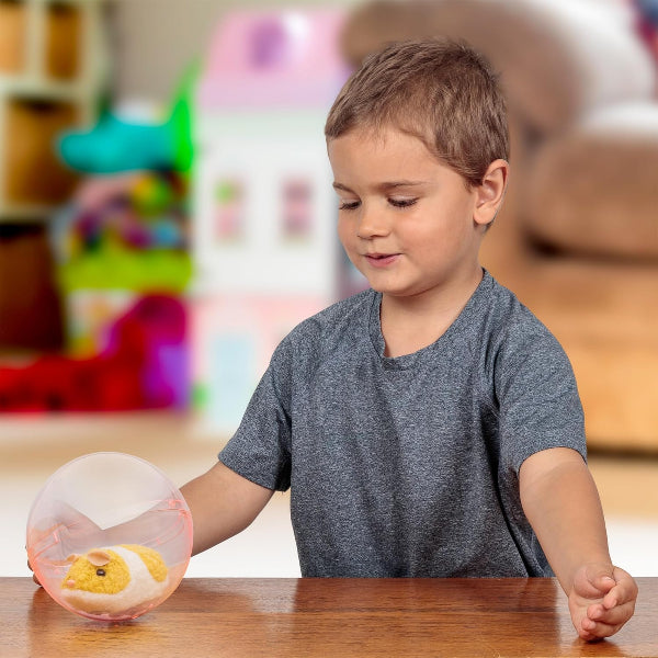Child playing with a small round transparent ball containing a hamster toy on a wooden table.