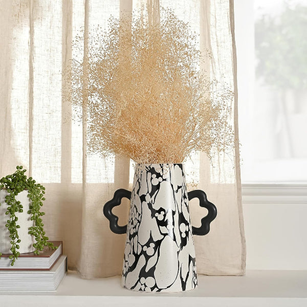 Black and white patterned vase with dried beige flowers against sheer curtains