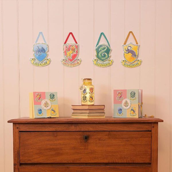 Four Harry Potter-themed house crests on a wall above a wooden chest with books and a lamp.