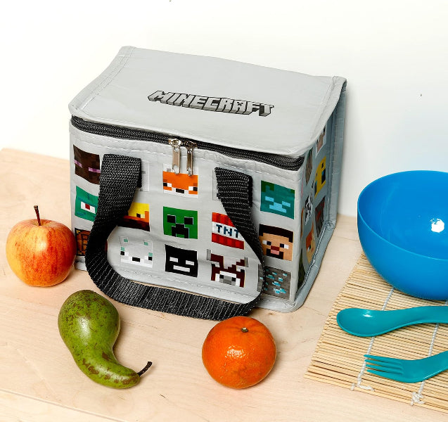 Gray Minecraft lunch bag with pixelated characters on a wooden surface with fruits and utensils.