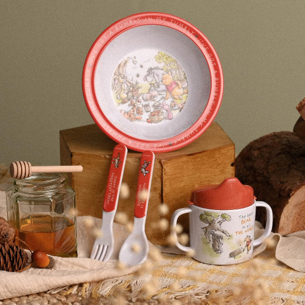 Children's tableware set with Winnie the Pooh design on a wooden surface.