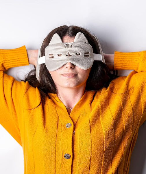 Person wearing a gray cat-eye sleep mask with a yellow sweater on a white background