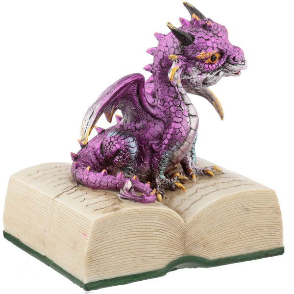 Purple dragon figurine on an open book with a white background