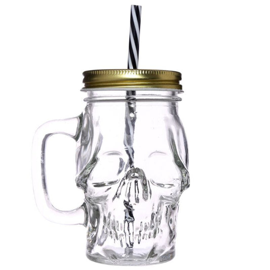 Clear skull-shaped glass mug with a gold lid and black and white straw on a white background