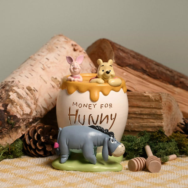 Decorative figurine with Winnie the Pooh, Piglet, and Eeyore around a honey pot with 'Money for Hunny' text, set against a wooden log background.