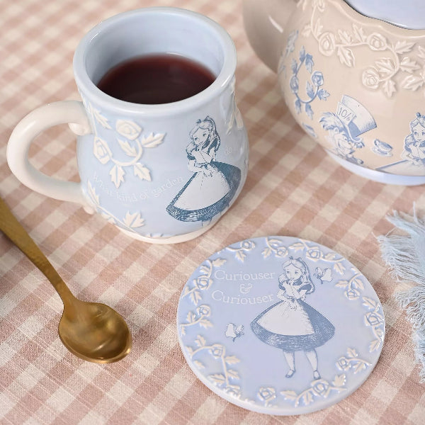 Ceramic mug and coaster with Alice in Wonderland design on a checkered tablecloth.