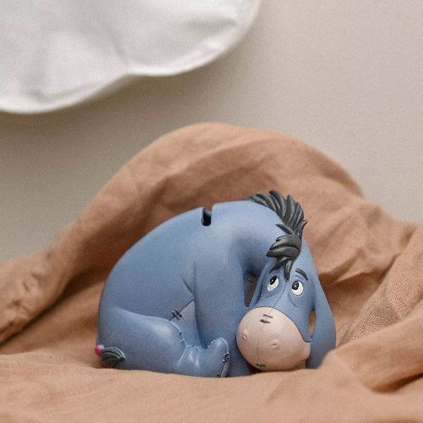 Blue cartoon character toy lying on a brown blanket with a white pillow in the background