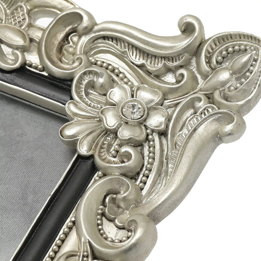 Decorative silver photo frame with intricate designs and a gemstone.