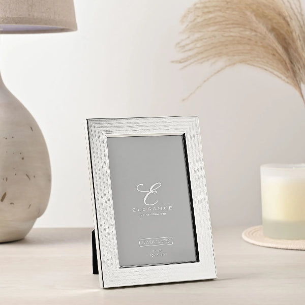 Silver photo frame with 'Elegance' branding on a decorative surface.