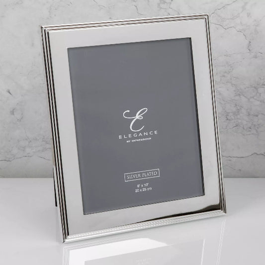 A silver-plated picture frame with a standing easel design, shown on a white reflective surface against a light gray marble background. The frame is empty, displaying a dark gray placeholder insert with the brand name 'ELEGANCE' and size details.