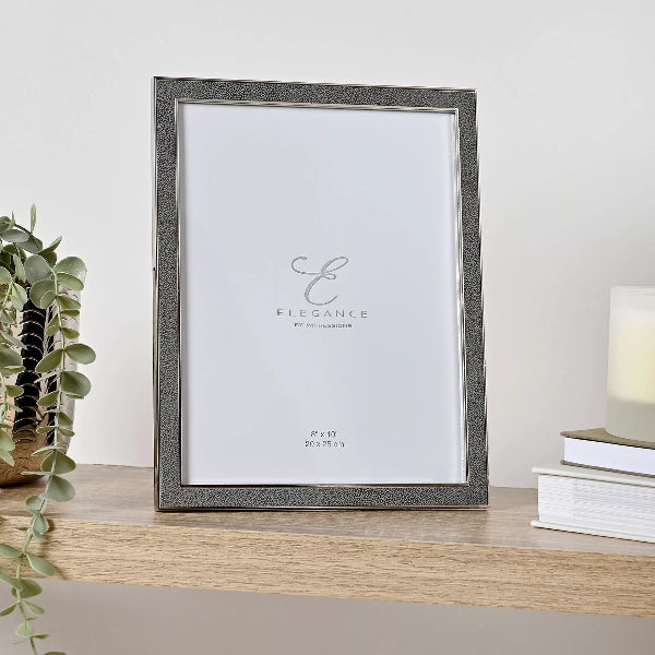 Gray photo frame on a wooden surface with a plant and books in the background