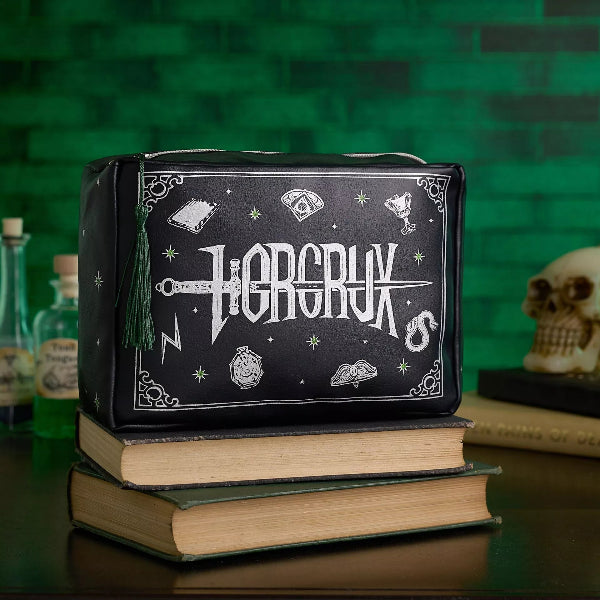 Black pouch with 'Horcrux' design on top of books against a green brick wall.
